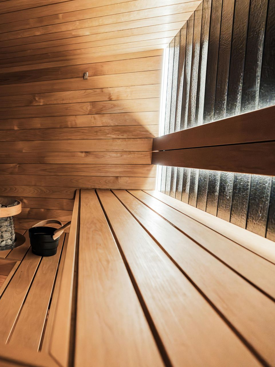 Wooden sauna interior with bench, plank walls, and a heater with stones on the left
