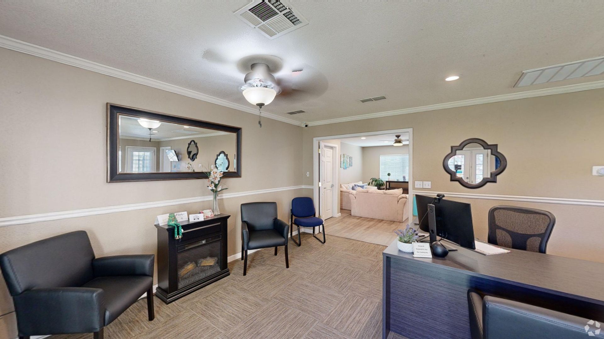 Reception area with chairs, desk, mirror, and a view into a living space. Beige walls and carpet.
