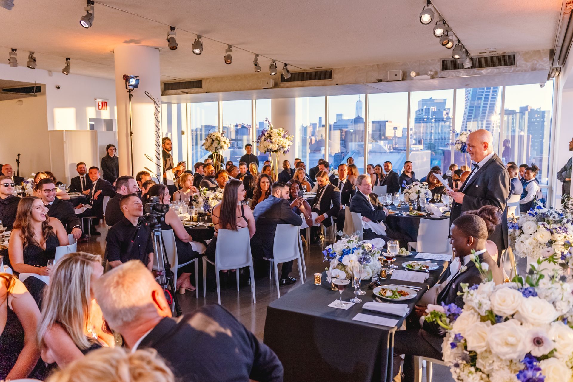 a man is giving a speech to a large group of people at a wedding reception .