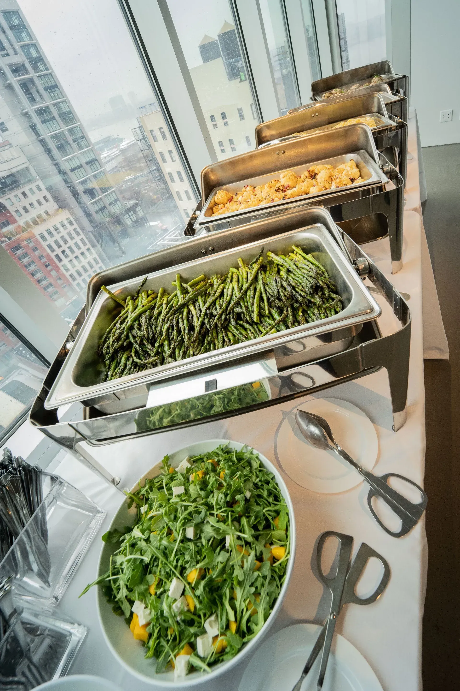 A buffet table with a variety of food and a bowl of salad.