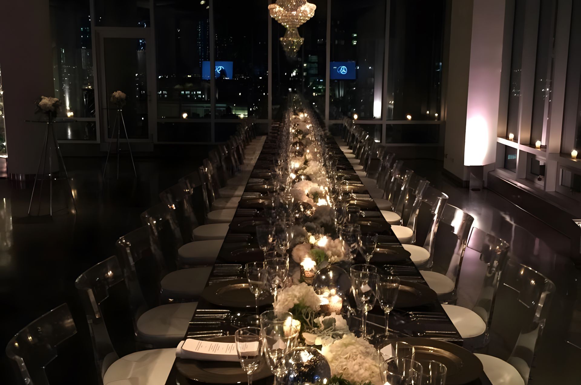 A long table with plates , glasses and candles in a dark room.
