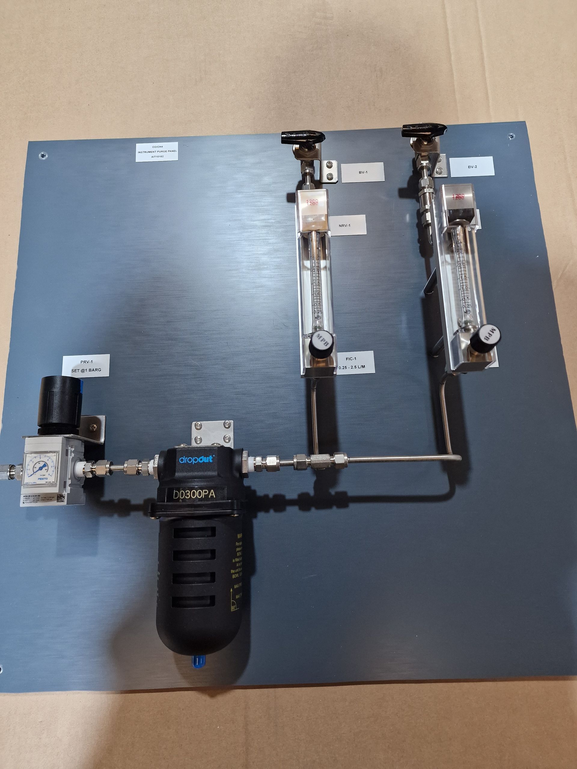 A laboratory gas manifold assembly on a gray panel, featuring two flow meters, a pressure regulator, and a filter.