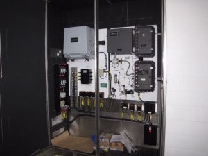 Industrial electrical control panel housed in a metal cabinet featuring various gray boxes, wiring, and switches.