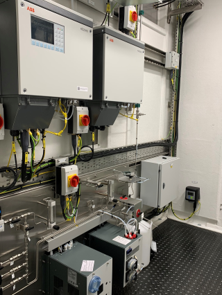 Two industrial ABB monitoring units mounted on a white wall above scientific equipment in a laboratory setting.