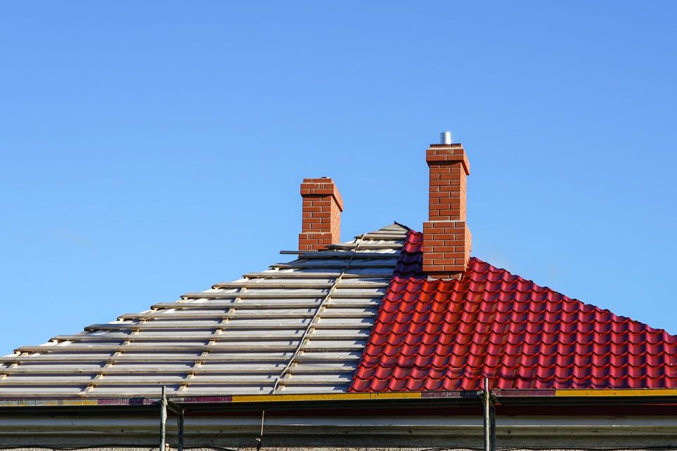 Red and gray tiled roof with two brick chimneys against a clear blue sky