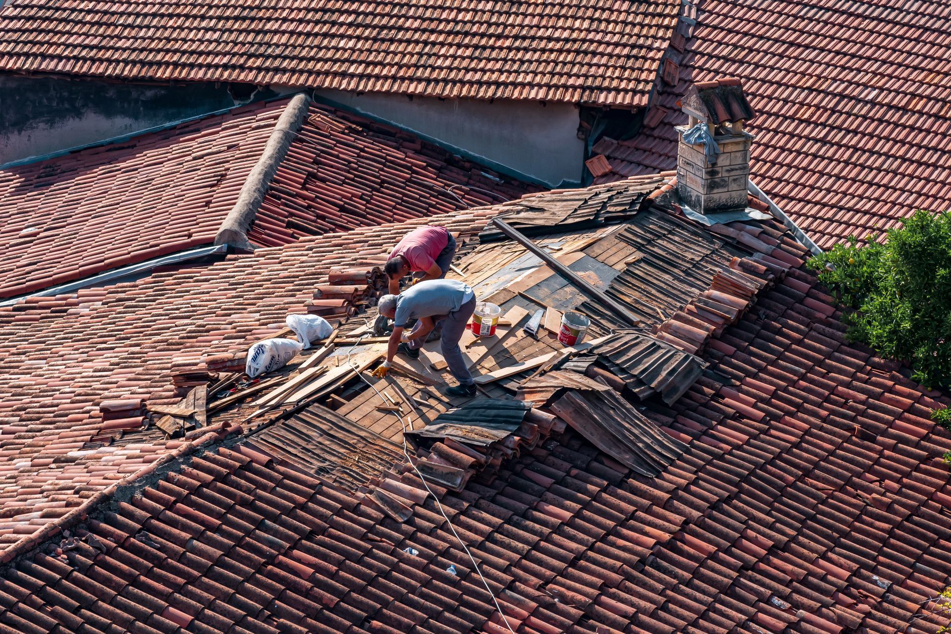 Workers repairing a damaged red-tile roof on a house