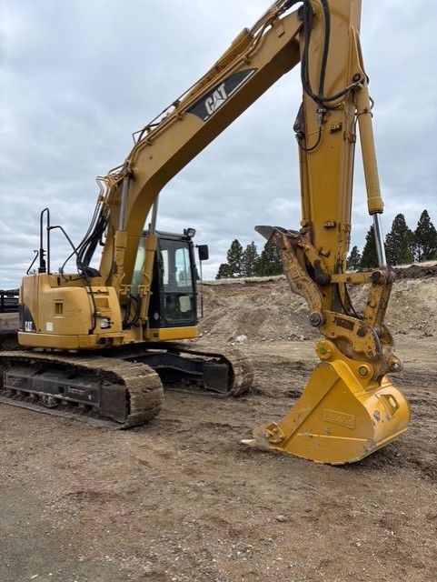 A yellow Caterpillar hydraulic excavator parked on a dirt lot under an overcast sky.