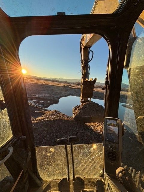 View from the cab of an excavator looking at a pond during a sunset.