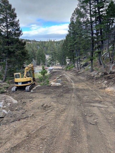 A yellow Caterpillar excavator parked on a dirt path in a wooded mountain area.