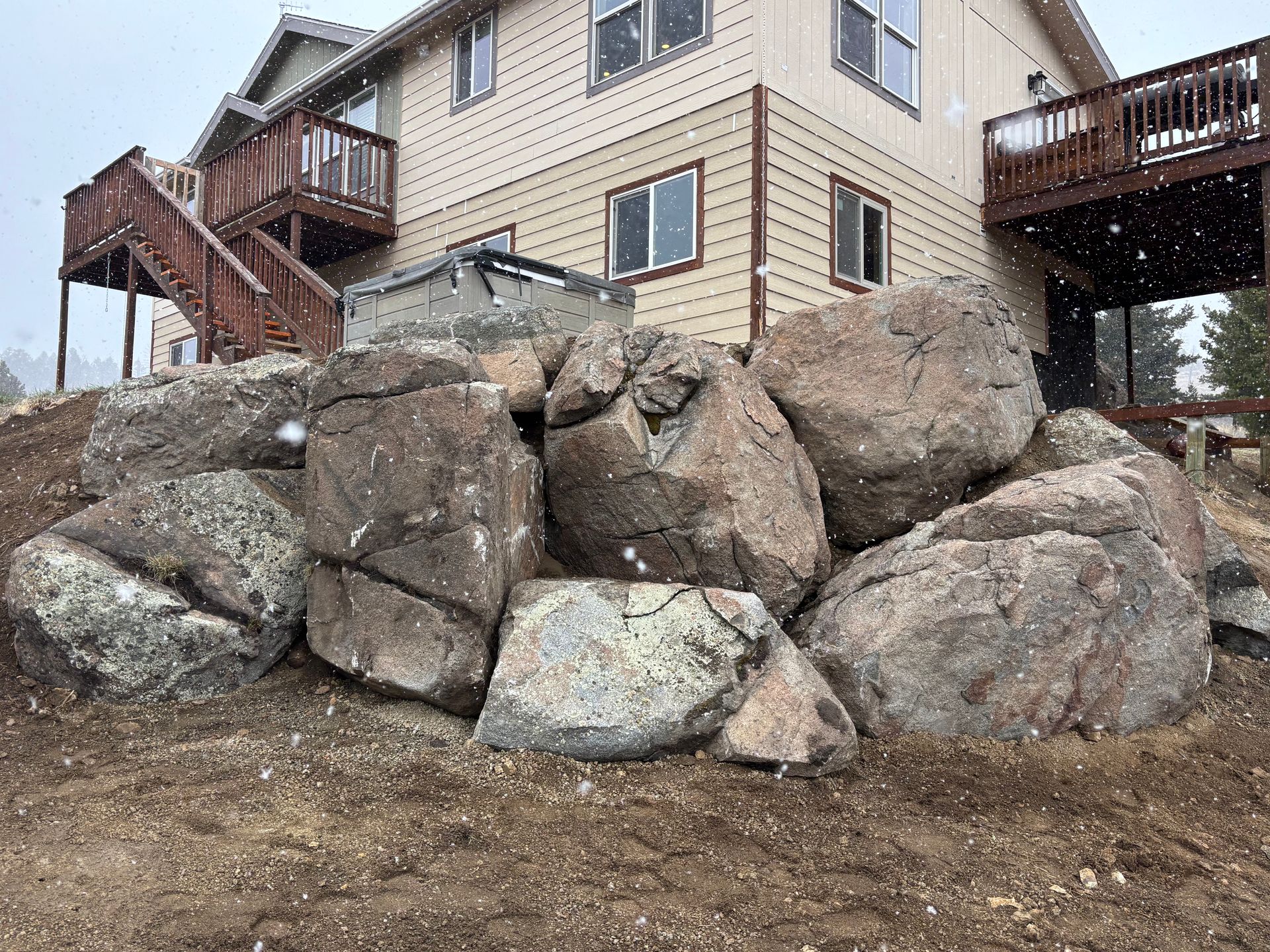House with wooden decks behind large boulders on a rocky hillside