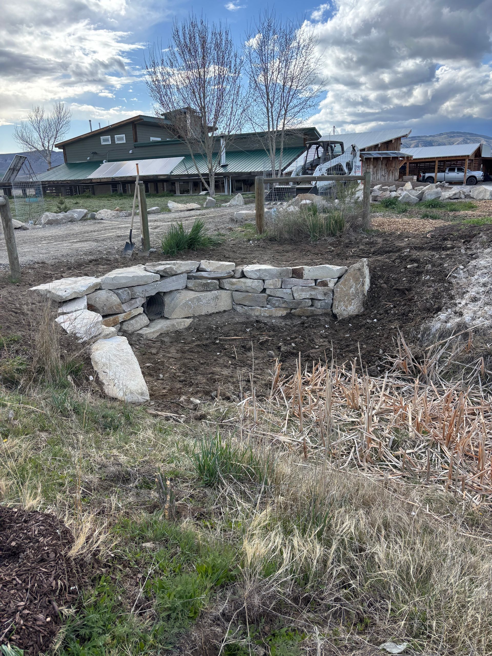 Stone fire pit in a dry yard with houses and bare trees in the background.