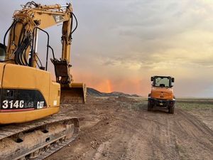 A yellow CAT excavator parked on a dirt slope in a wooded area.