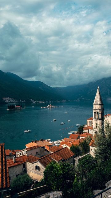 Red-roofed lakeside town with a church steeple, blue water, and misty mountains under cloudy sky