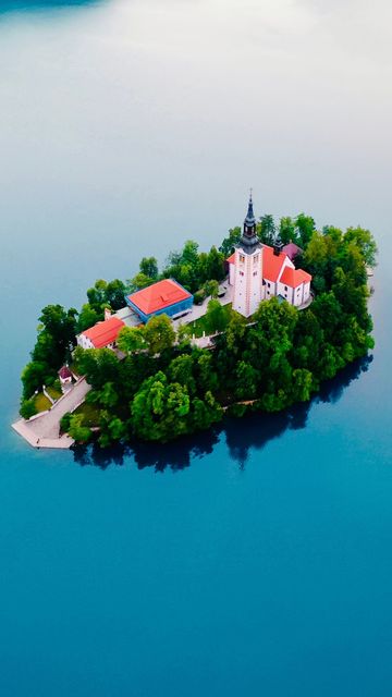 Small island with a pink church and green trees surrounded by calm blue water.