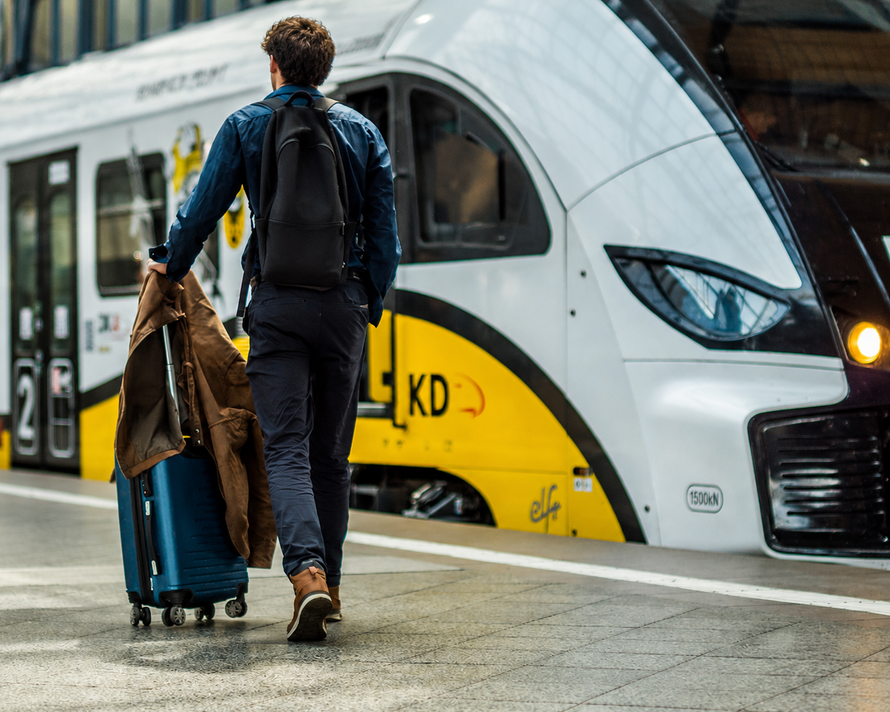 Traveler pulling a blue suitcase beside a white-and-yellow train at the station