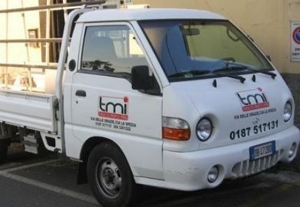 Camion per le consegne TMI bianco parcheggiato all’aperto, visto di lato, con il logo aziendale e il numero di telefono visibili