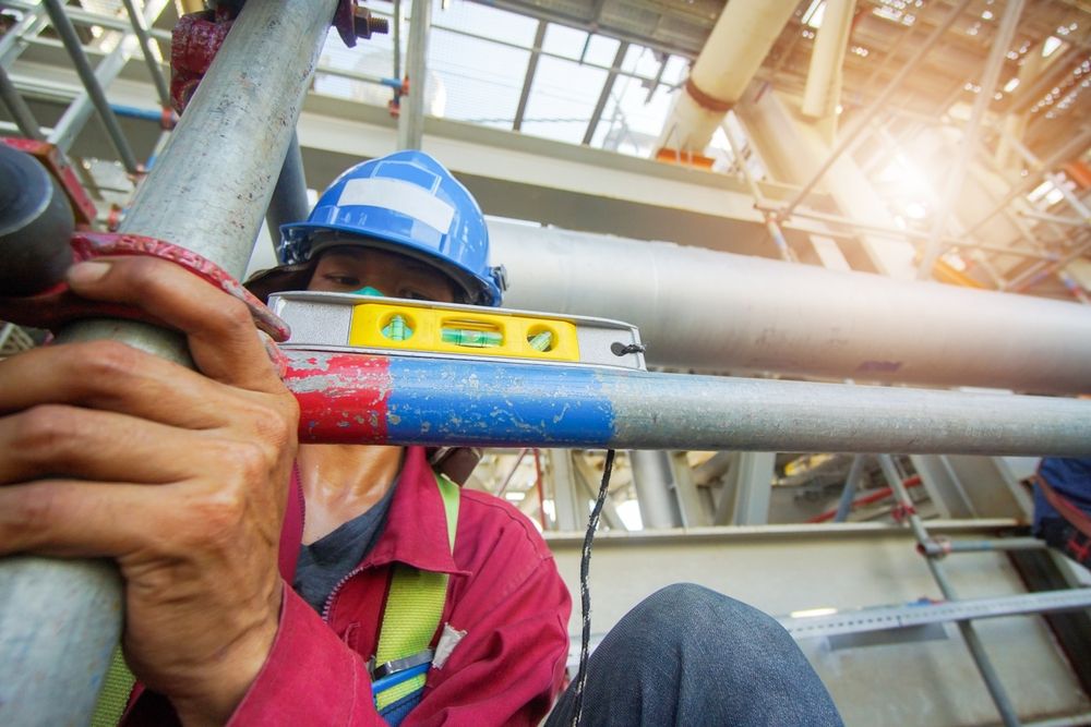 A Construction Worker is Using a Level to Measure a Pipe — Byron Bay Scaffold in Alstonville, NSW