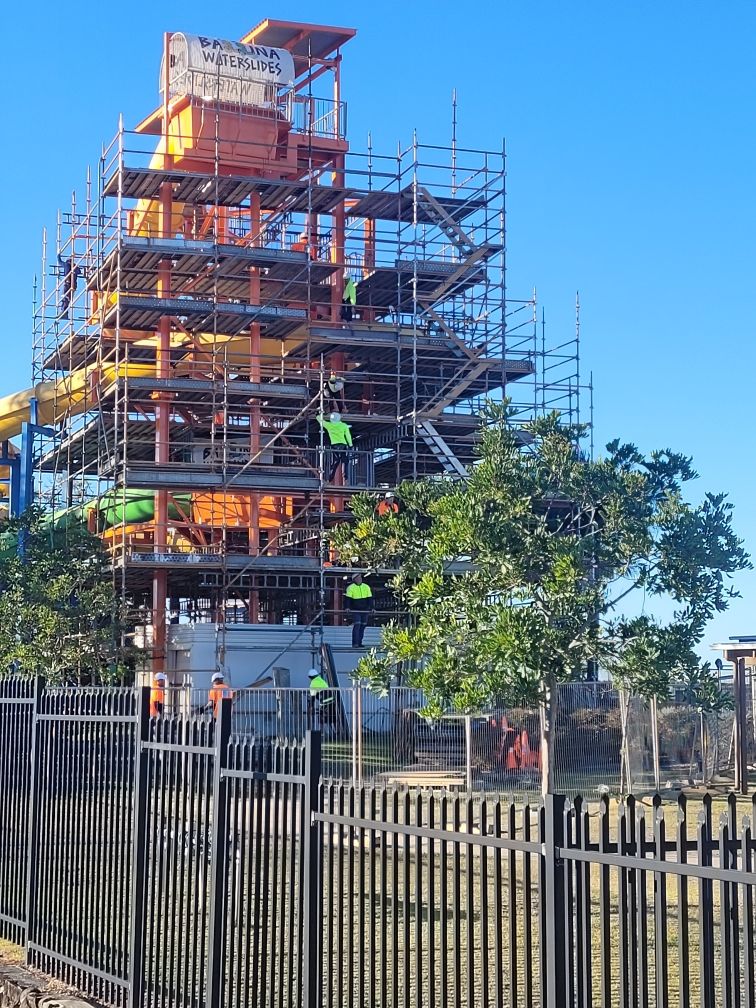 A tall orange water slide under construction, surrounded by scaffolding. Workers in safety vests are visible.-Byron Bay Scaffold in Kinvara, NSW
