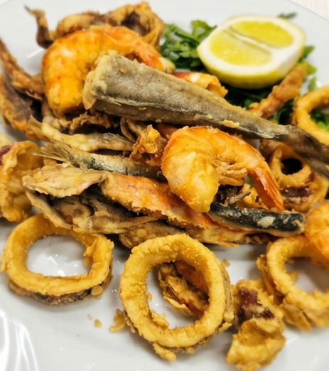 Piatto di frutti di mare fritti con gamberi, anelli di calamari, pesce e spicchi di limone su un piatto bianco.