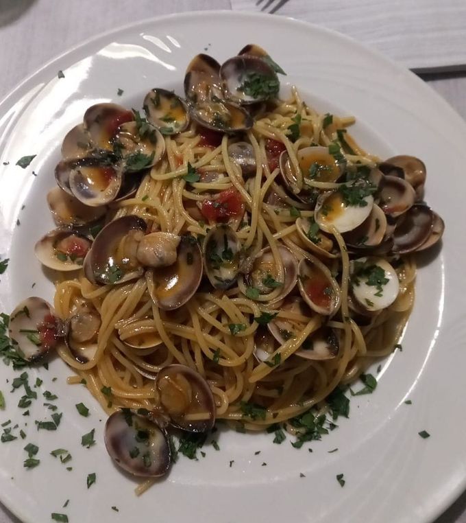 Piatto di spaghetti con vongole, pomodorini e prezzemolo su una tovaglia bianca.