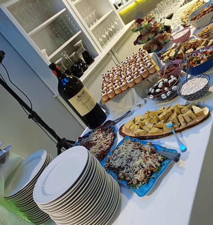 Tavolo da buffet con vino, piatti impilati e assaggi assortiti su vassoi bianchi.