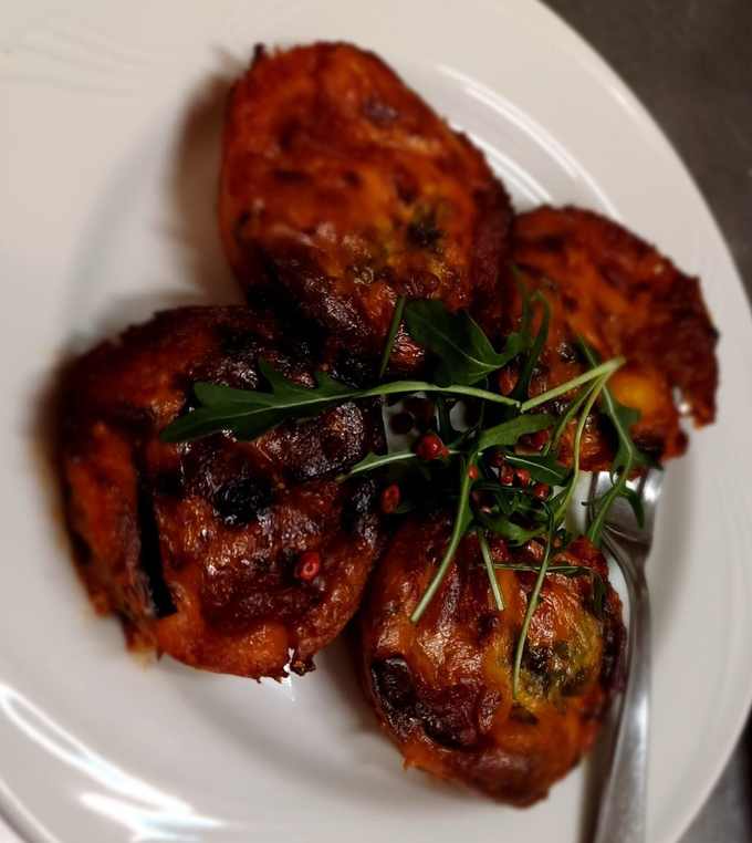 Quattro pezzi di pollo arrosto glassati su un piatto bianco, guarniti con erbe aromatiche fresche.