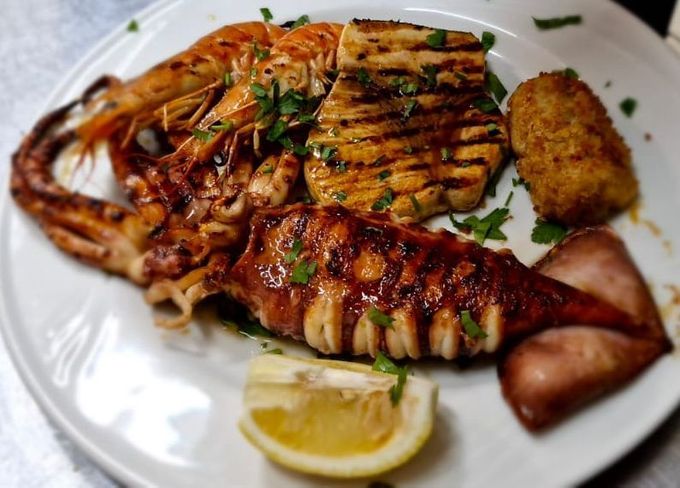 Piatto di frutti di mare grigliati con aragosta, pesce, patatine fritte e limone su un piatto bianco.