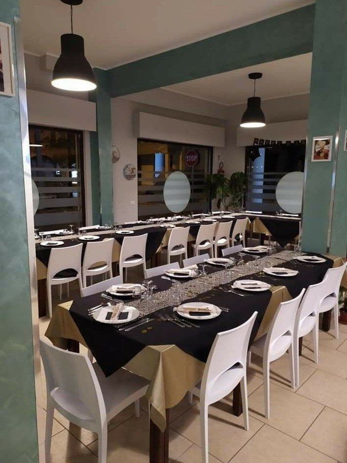 Allestimento della sala da pranzo in un ristorante con apparecchiatura della tavola in bianco e nero, sedie bianche e pareti color verde acqua.