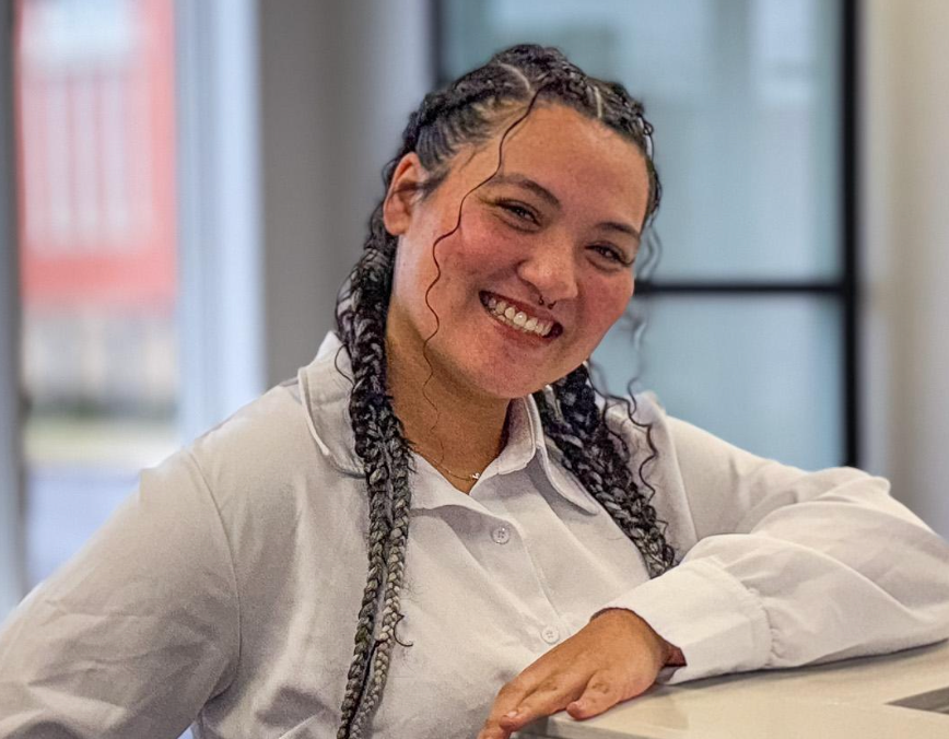 A woman with braids is smiling and leaning on a counter.