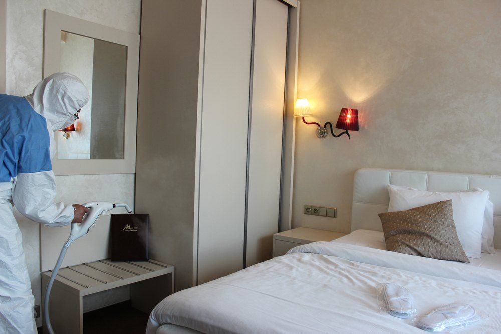 Person in Hazmat Suit Disinfecting a Hotel Room With a Sprayer — Optimum Pest Services In Palm Cove, QLD