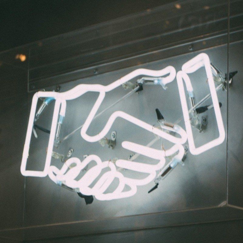 A neon sign of two hands shaking each other