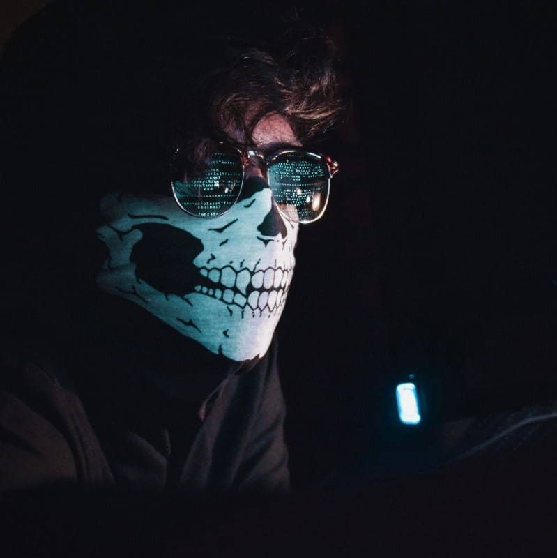 A man wearing a skull mask and sunglasses is using a cell phone.