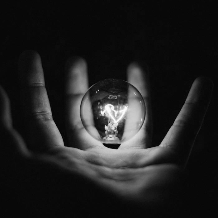A person is holding a light bulb in their hands in a black and white photo.