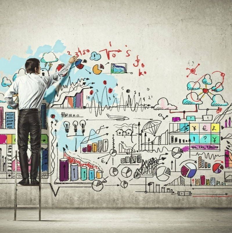 A man is standing on a chair drawing on a wall
