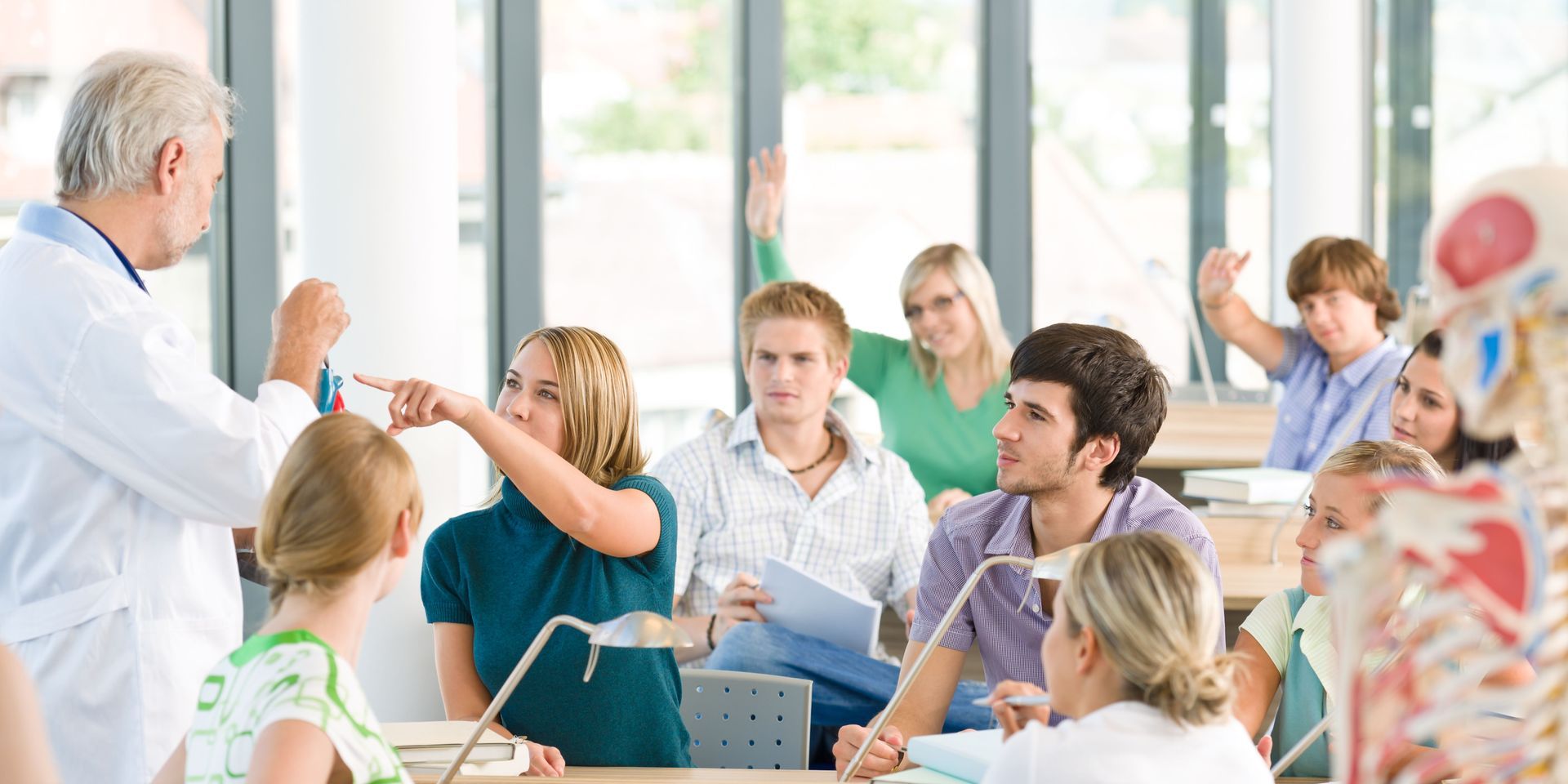 A group of students are sitting in a classroom with their hands up.