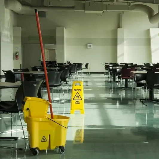 Mensa vuota con tavoli e sedie, secchio giallo per la pulizia e cartello di avvertimento pavimento bagnato sul pavimento riflettente.