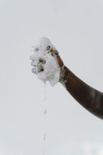Lavaggio delle mani con sapone schiumoso, gocce d'acqua che cadono da una mano alzata su uno sfondo neutro.