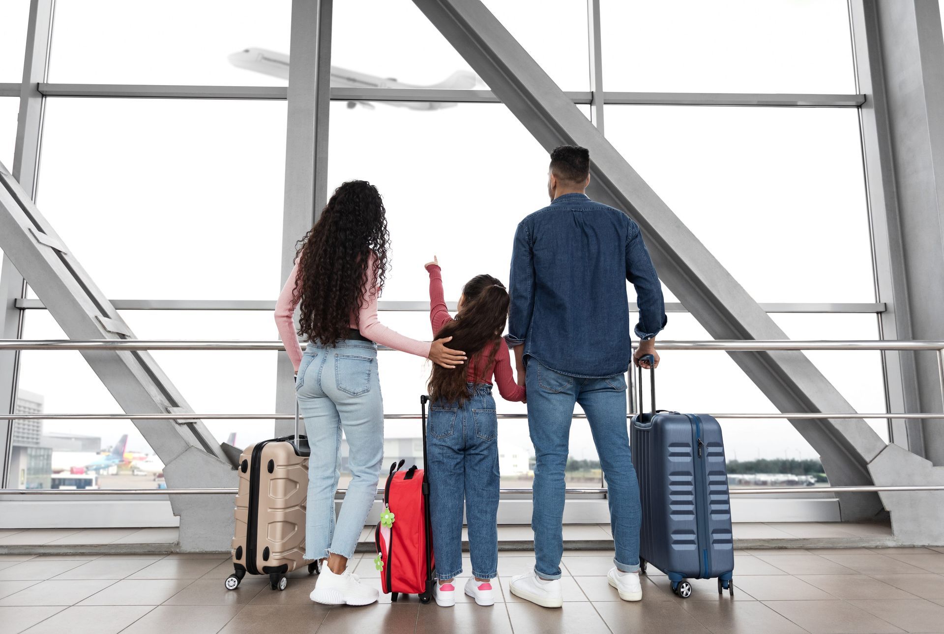 Family with luggage standing in an airport terminal, seen from behind.