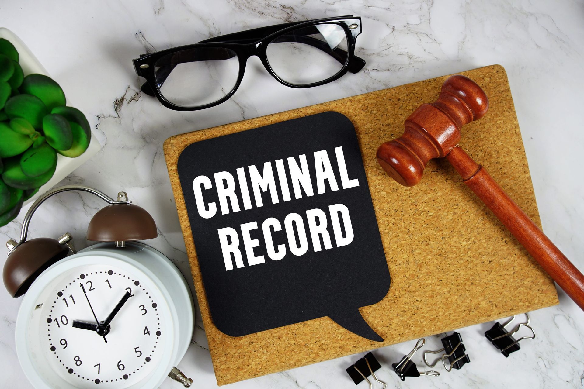 Criminal record file beside gavel, eyeglasses, and clock on a desk
