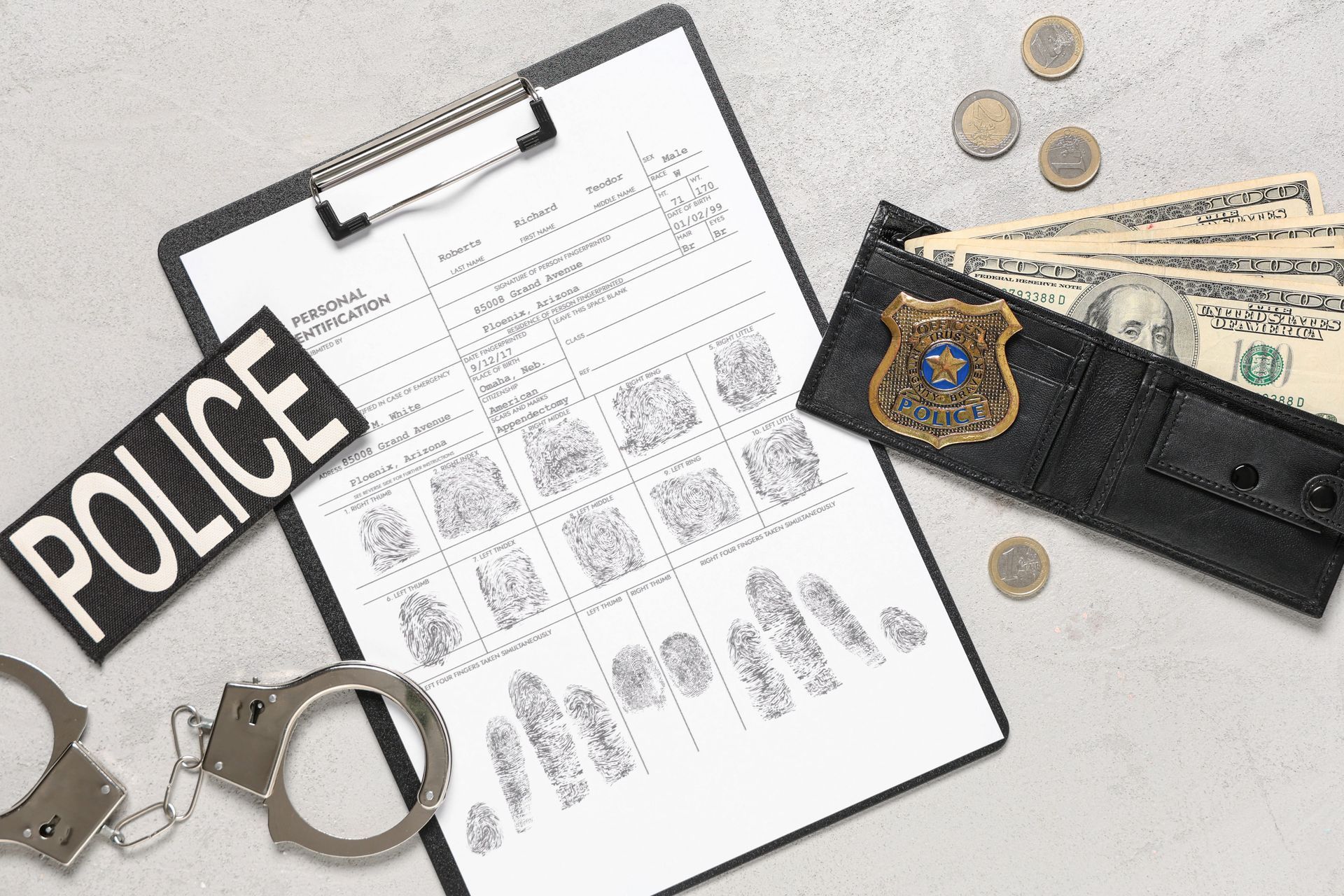 Police evidence board with fingerprint sheet, handcuffs, badge, cash, and a black notebook on a white surface