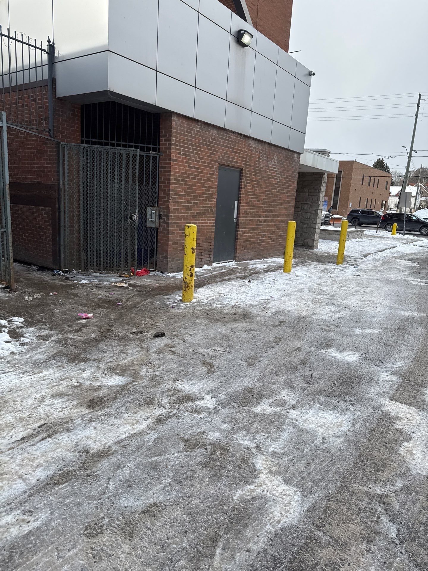 A snowy sidewalk in front of a brick building with yellow poles.