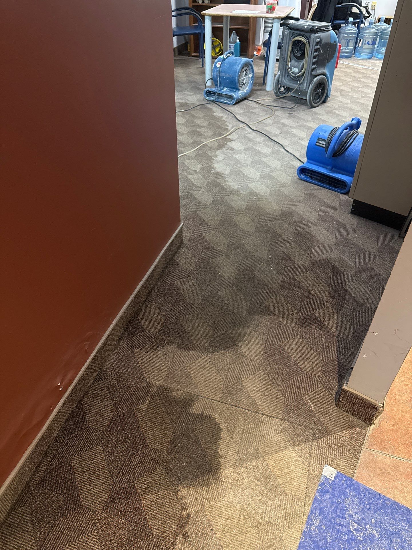A room with a lot of water on the floor and a vacuum cleaner on the floor.