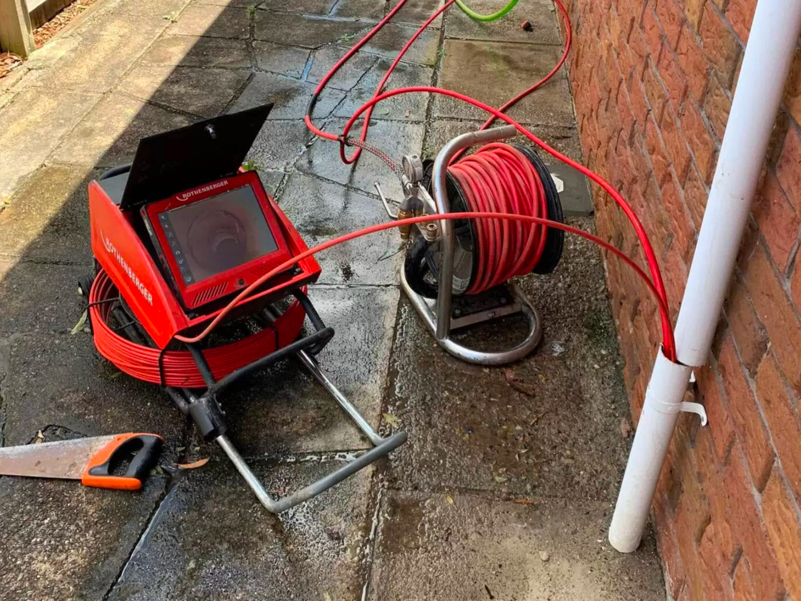 Red cable reel and portable light on wet pavement beside a brick wall
