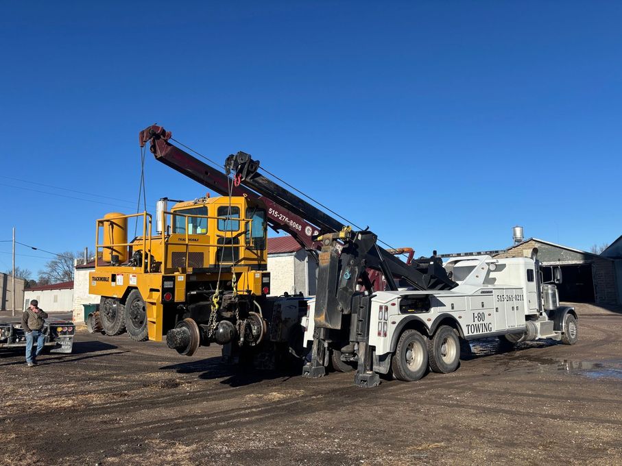 Yellow crane truck and white utility truck parked on dirt under a clear blue sky