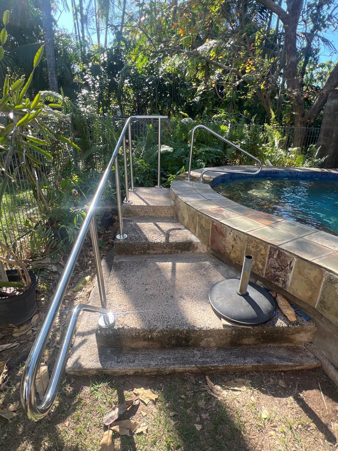 Stone steps with metal handrails leading to a pool. Lush greenery surrounds the pool area — Friendly Pool & Spa Care in Palmerston, NT