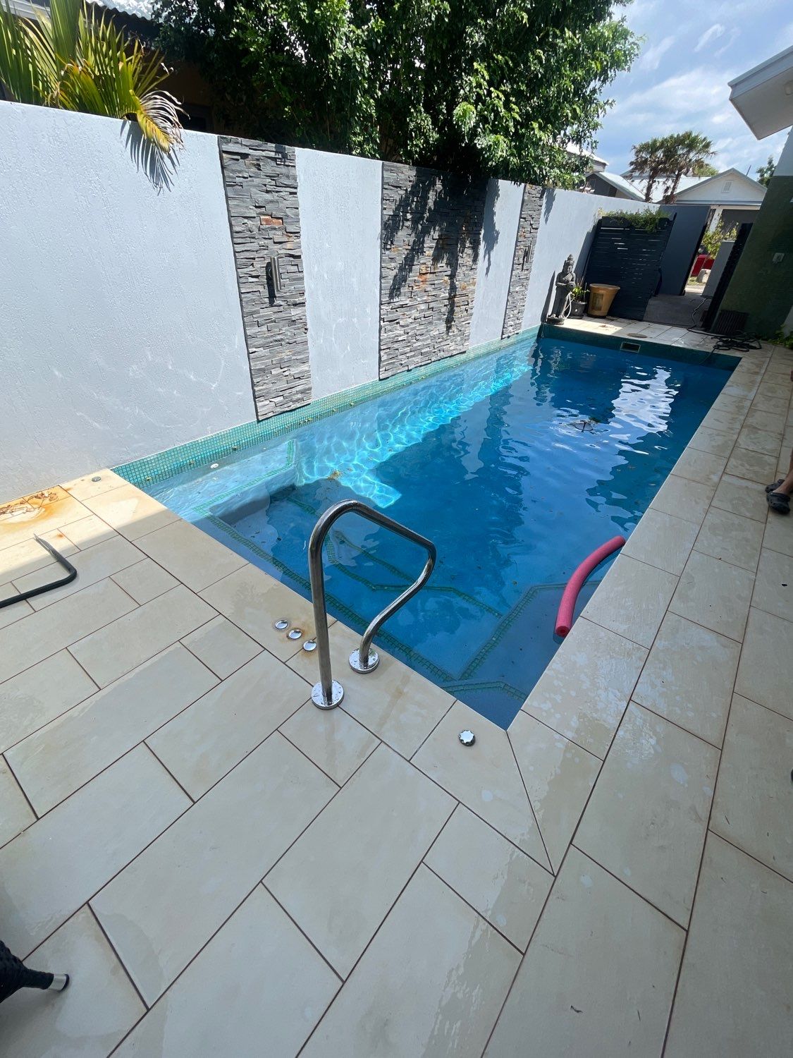Small rectangular pool with blue water. Cream-colored stone patio. Decorative wall with gray stone inserts — Friendly Pool & Spa Care in Coconut Grove, NT