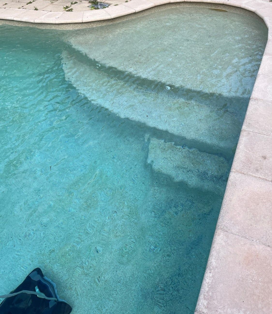 Light blue water fills a swimming pool with tiered steps leading into the shallow end, bordered by beige stone coping — Friendly Pool & Spa Care in Coconut Grove, NT