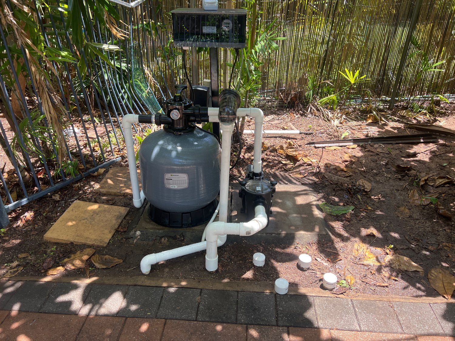 Pool filter system in a backyard, with grey tank, white pipes, and a black pump — Friendly Pool & Spa Care in Coconut Grove, NT