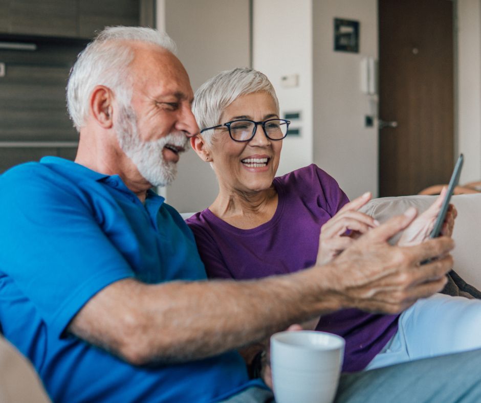 An elderly couple is sitting on a couch looking at a cell phone.