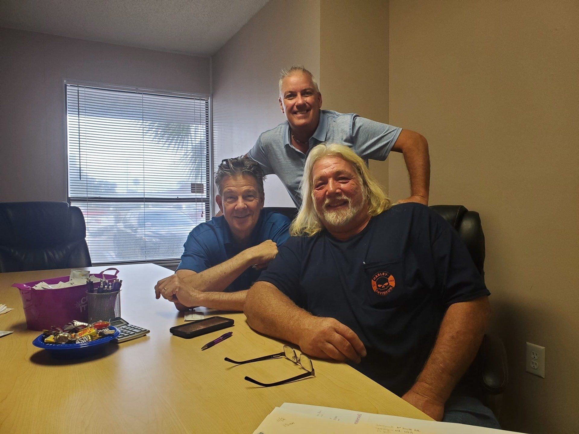 Three men are posing for a picture while sitting at a table.